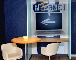 Una habitación con una pantalla grande que muestra 'INTERNET' y una flecha apuntando a la izquierda, una mesita redonda con un bol y dos sillas.