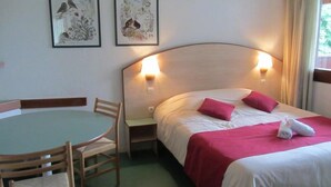 A hotel room with a bed, a table with chairs, and two wall-mounted lamps. - Vvf Villages Parent (Parent)