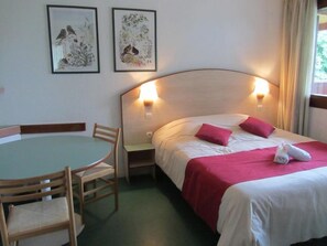 A hotel room with a bed, a table with chairs, and two wall-mounted lamps. - Vvf Villages Parent (Parent)