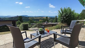 A patio with two chairs and a table, overlooking a scenic landscape with hills and a body of water. - Vvf Villages Parent (Parent)