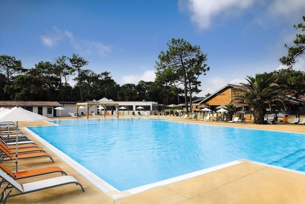 Una piscina grande con sillones de descanso y sombrillas, rodeada de árboles y edificios.