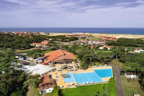 Vista aérea de un complejo turístico costero con piscina, playa y vegetación circundante.