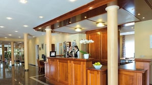 Zona de recepción de un hotel con un mostrador de madera, un jarrón blanco con flores y un suelo de mármol.