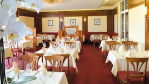 Un comedor de hotel con mesas preparadas para los huéspedes, una araña y cuadros en las paredes.