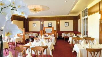 A hotel dining area with tables set for guests, a chandelier, and framed artwork on the walls.