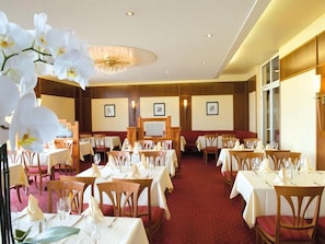 A hotel dining area with tables set for guests, a chandelier, and framed artwork on the walls. - Victor S Residenz Teistungenburg (Teistungen)