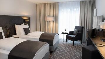 A hotel room with two beds, a desk, a chair, a television, and a lamp.