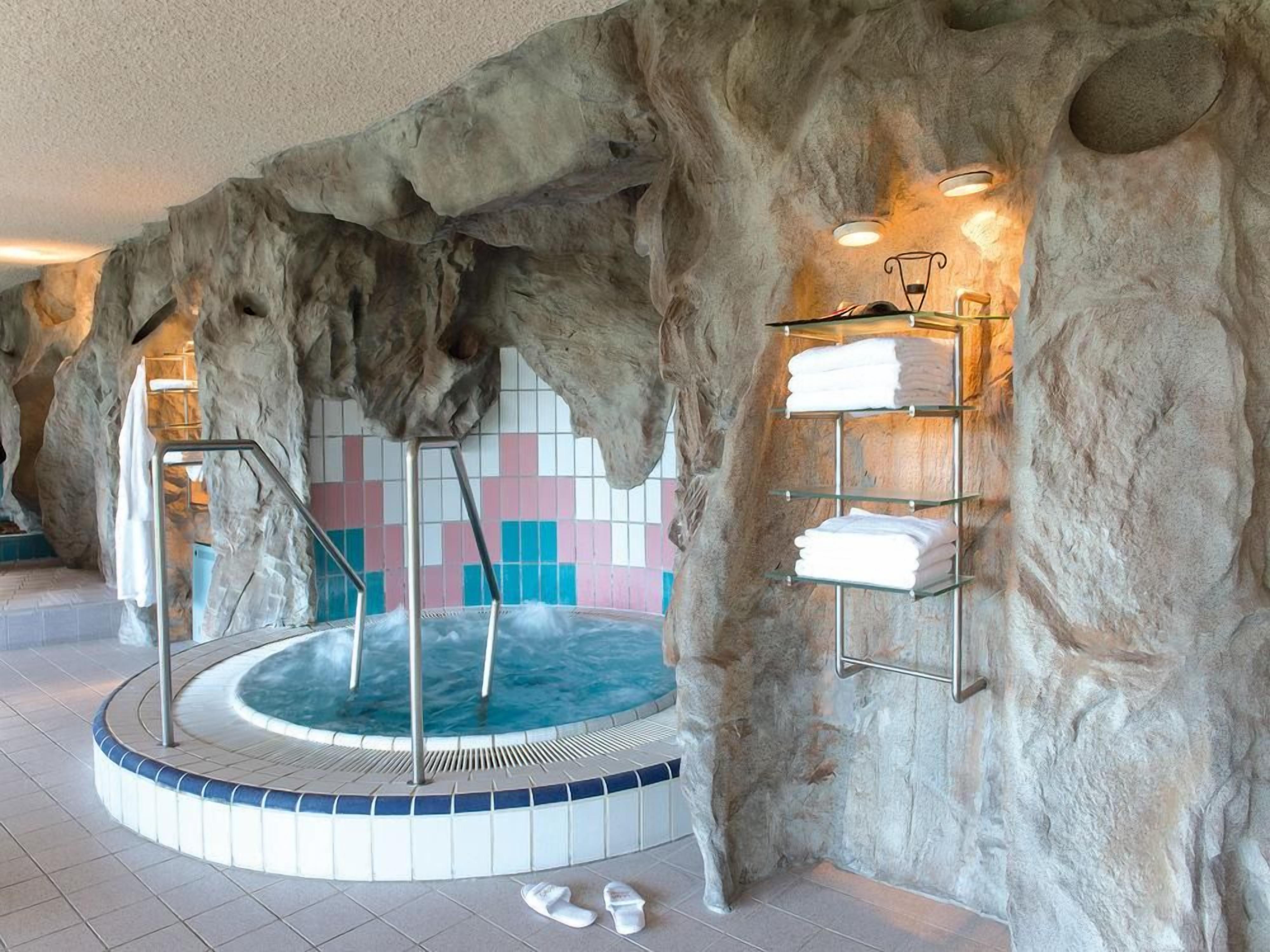 A spa area with a hot tub, tiled walls, and shelves with towels.
