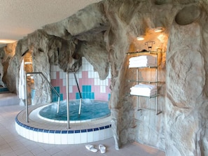 A spa area with a hot tub, tiled walls, and shelves with towels. - Victor S Residenz Teistungenburg (Teistungen)