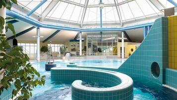 An indoor swimming pool with a glass ceiling, blue tiles, and a central water feature.