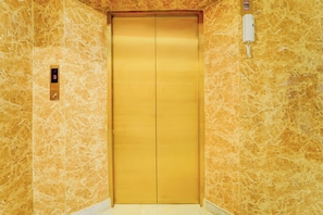 A gold elevator in a hallway with marble walls and a digital elevator call button.