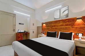 Ein Hotelzimmer mit Bett, Nachttischen, einem Holz-Kopfteil, Kunstwerken an der Wand und einer Minibar.