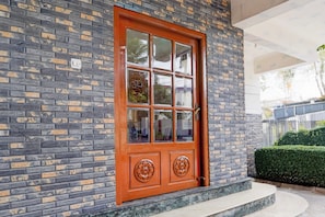 A brick building with a large wooden door featuring a glass panel and decorative metal handles.