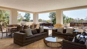 An outdoor patio with wicker furniture, a round table, and a stone fireplace. - Zebula Golf Estates & Spa (Bela-Bela)