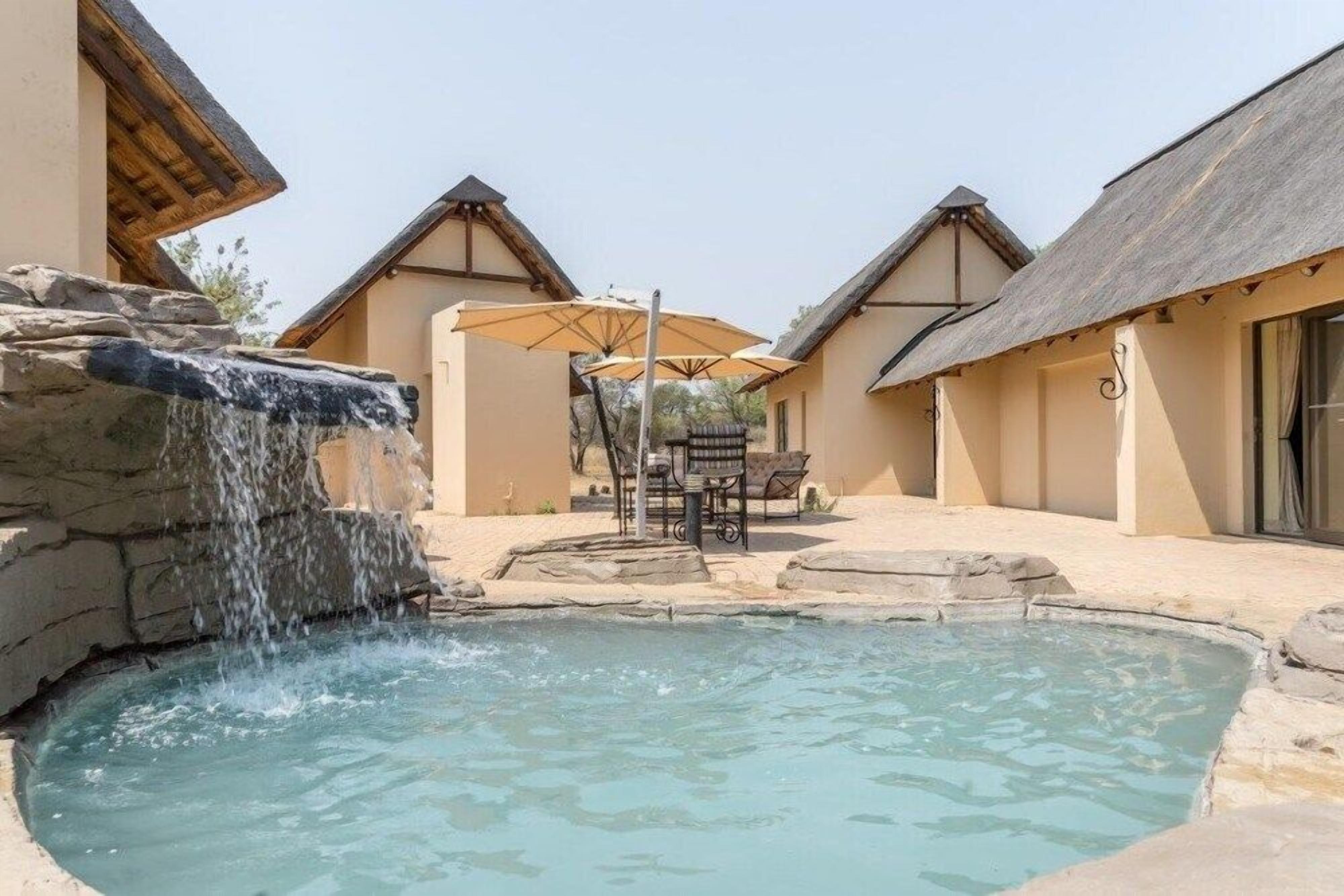 A pool area with a waterfall feature, outdoor seating, and traditional architecture.