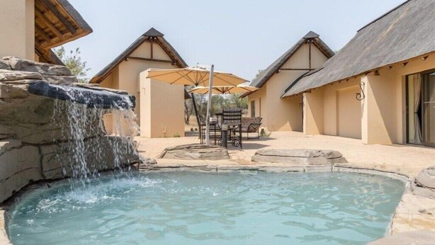 A pool area with a waterfall feature, outdoor seating, and traditional architecture. - Zebula Golf Estates & Spa (Bela-Bela)