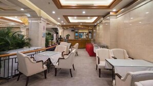 Un hall d’hôtel comprenant un comptoir d’accueil, un espace détente avec des tables et des chaises, et un plafond décoratif.
