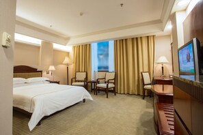 Ein Hotelzimmer mit einem großen Bett, zwei Stühlen, einem Schreibtisch und einem Fernseher.