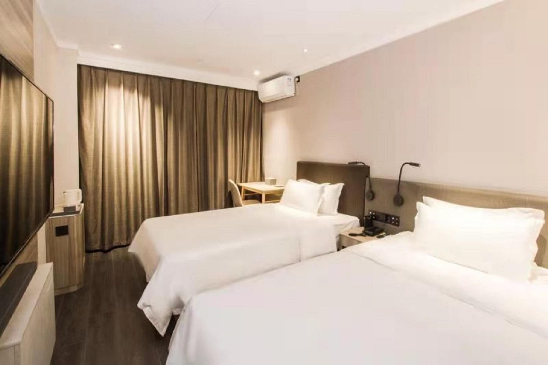 A hotel room with two beds, a desk, a chair, a lamp, and an air conditioning unit.