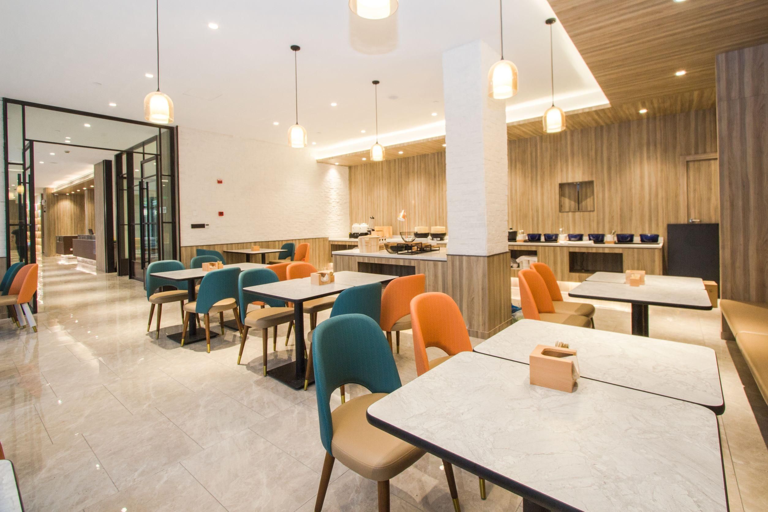 A modern restaurant interior with multiple dining tables and chairs, a kitchen area, and a glass partition separating the dining area from the kitchen.