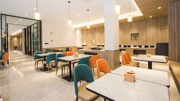 A modern restaurant interior with multiple dining tables and chairs, a kitchen area, and a glass partition separating the dining area from the kitchen.