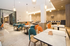 Un intérieur de restaurant moderne, avec plusieurs tables et chaises, un espace cuisine et une cloison en verre séparant la salle à manger de la cuisine.