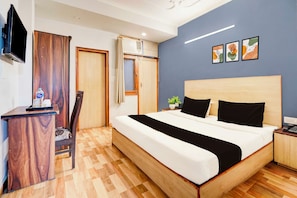 Una habitación de hotel con cama, escritorio, silla, televisor y obras de arte en la pared.