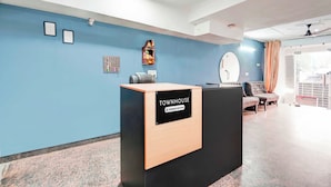 Een receptiebalie met de aanduiding 'TOUMHOUSE Company Serviced', een blauwe muur, ingelijste foto's, een klein altaartje en een zithoek met een ronde spiegel.
