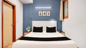 Een hotelkamer met een groot bed, een nachtkastje, een potplant en een spiegel aan de muur.