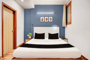Habitación de hotel con una cama grande, una mesita de noche, una planta en maceta y un espejo montado en la pared.