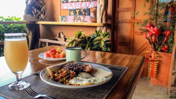 A breakfast setting with a plate of food, a glass of juice, and a mug on a table. - Santa Juana Lodge Nature Reserve (Naranjito)