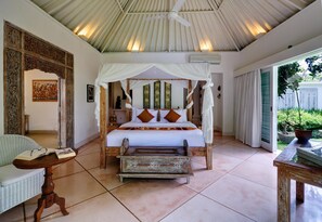 A bedroom with a four-poster bed, a wooden bench, a wicker chair, and a ceiling fan. - Villa Sipo (Keroboken Kelod)