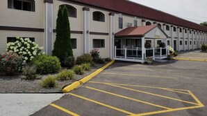 A motel with a covered entrance, a parking lot, and a row of windows. - All Seasons Inn And Suites (Buzzards Bay)