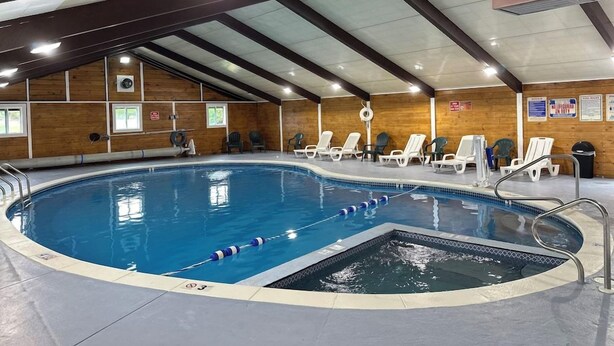 An indoor swimming pool with a diving area, surrounded by lounge chairs and a wooden wall. - All Seasons Inn And Suites (Buzzards Bay)