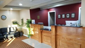 A reception area with a wooden reception desk, a black leather couch, and a potted plant. - All Seasons Inn And Suites (Buzzards Bay)