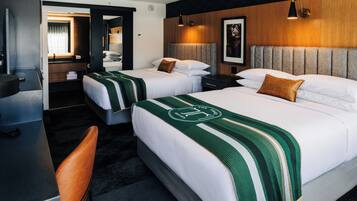 A hotel room with two beds, a desk, a chair, and a bathroom visible through an open door.