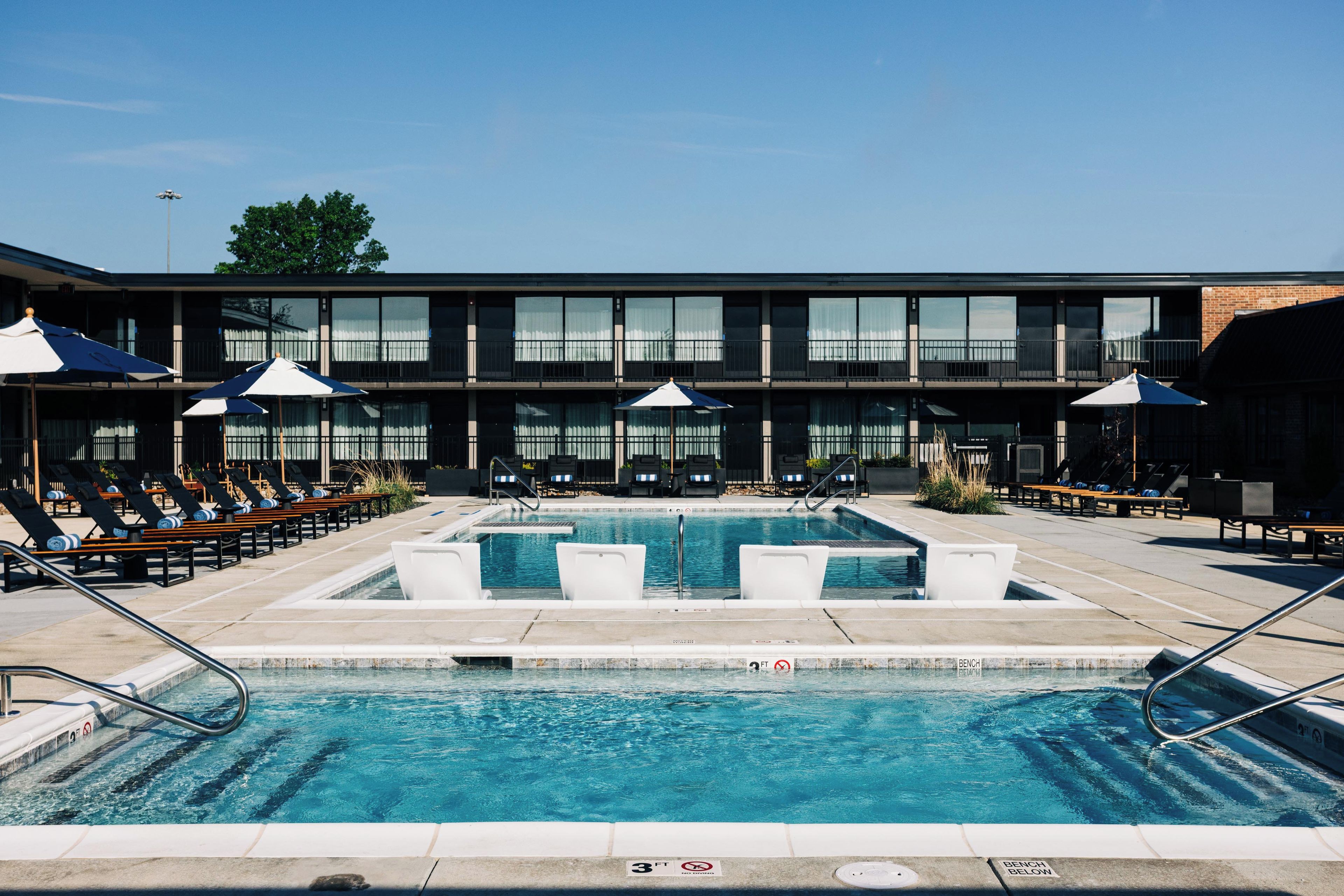 A pool area with lounge chairs and umbrellas, a building with large windows, and a clear sky.