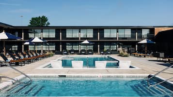A pool area with lounge chairs and umbrellas, a building with large windows, and a clear sky.