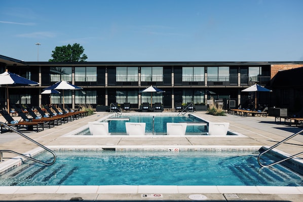 A pool area with lounge chairs and umbrellas, a building with large windows, and a clear sky. - Quality Inn Bardstown (Bardstown)