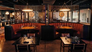 Un restaurante con cabinas y mesas, detalles de madera e iluminación colgante.