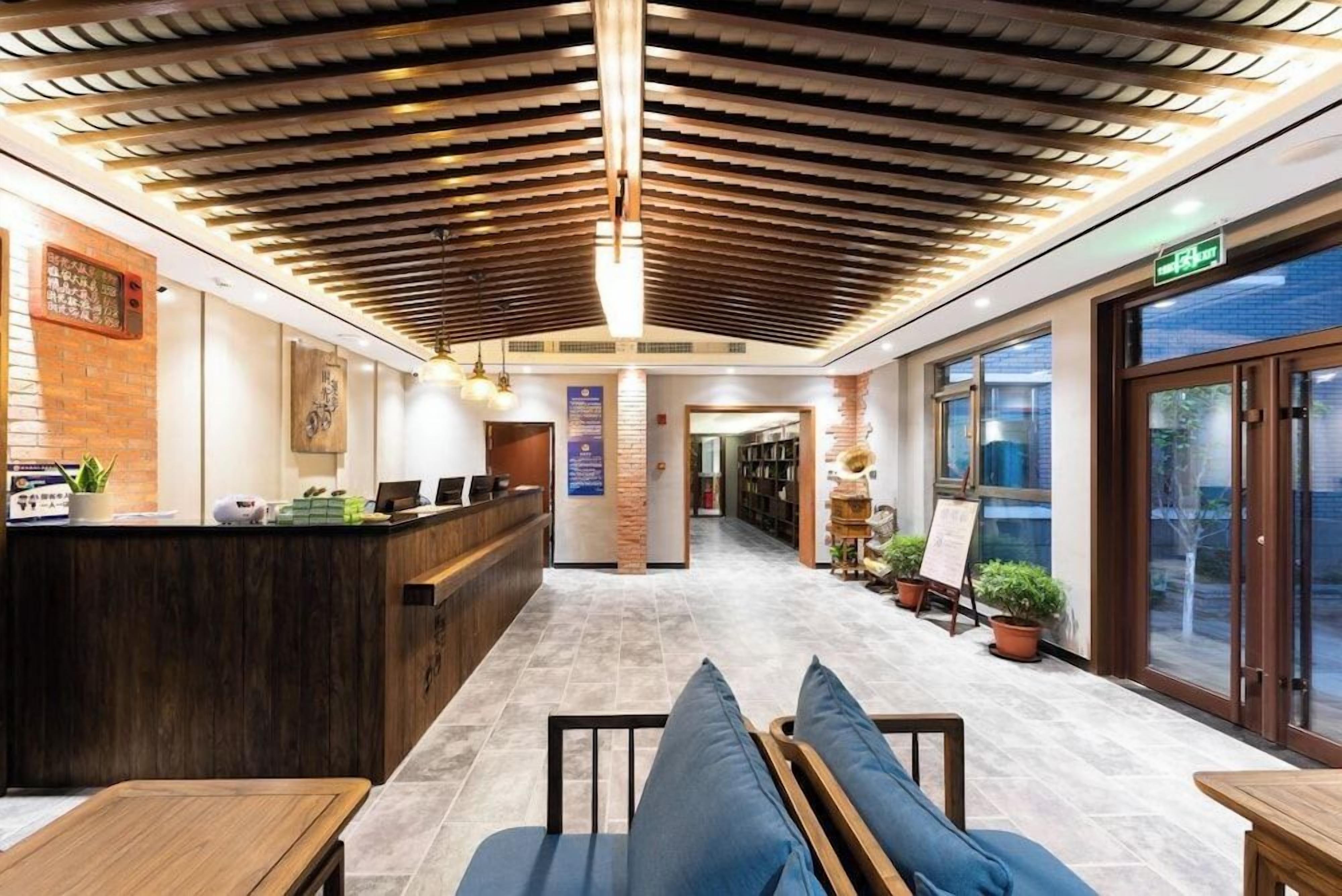 A hotel lobby with a reception desk, seating area, and a view through the glass doors.