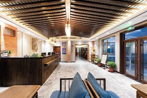 Un hall de hotel con una recepción, zona de estar y vistas a través de puertas de cristal.