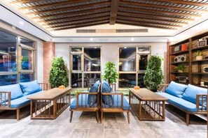 Un interior moderno con techo de madera, ventanas amplias y una zona de estar con cojines azules y mobiliario de madera.