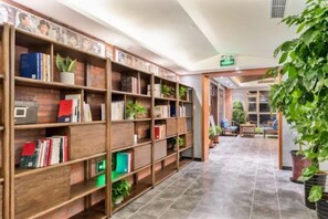 Una biblioteca con estanterías, suelo de baldosas y plantas en macetas.