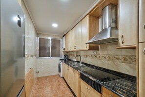 A kitchen with wooden cabinets, a stainless steel range hood, a built-in oven, and a washing machine. - Puerto Atarazanas Flat – Apartment in Valencia next to the Atarazanas (València)