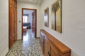 A hallway with a wooden cabinet, a patterned floor, and a door leading to a room with a sofa. - Puerto Atarazanas Flat – Apartment in Valencia next to the Atarazanas (València)