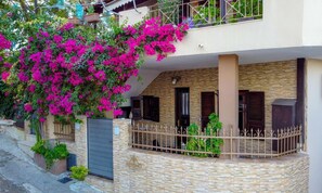 A two-story house with a stone facade, a balcony with a wrought iron railing, and a large flowering bush. - Kensho Skiathos Apartments (Skiathos)
