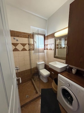 A bathroom with a shower, toilet, sink, and a washing machine. - Kensho Skiathos Apartments (Skiathos)