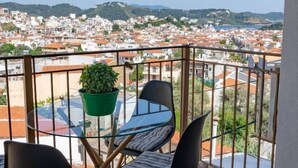 Un balcón con una mesa y sillas, una planta en maceta y vistas de la ciudad.