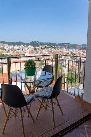 A balcony with a table and chairs, a potted plant, and a view of a cityscape. - Kensho Skiathos Apartments (Skiathos)